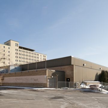 Élévation est de l'aréna Lassonde-Oasis. Toutes les façades du bâtiment sont aveugles et composées de matériaux sobres, soit la brique et la tôle. Photographie.